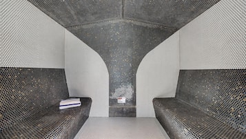 A room with a unique geometric ceiling design, a central seating area, and a warning sign indicating hot steam.