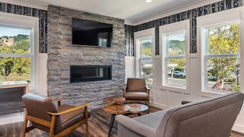 A modern living room with a stone wall, a flat-screen TV, and large windows offering a view of the outdoors.