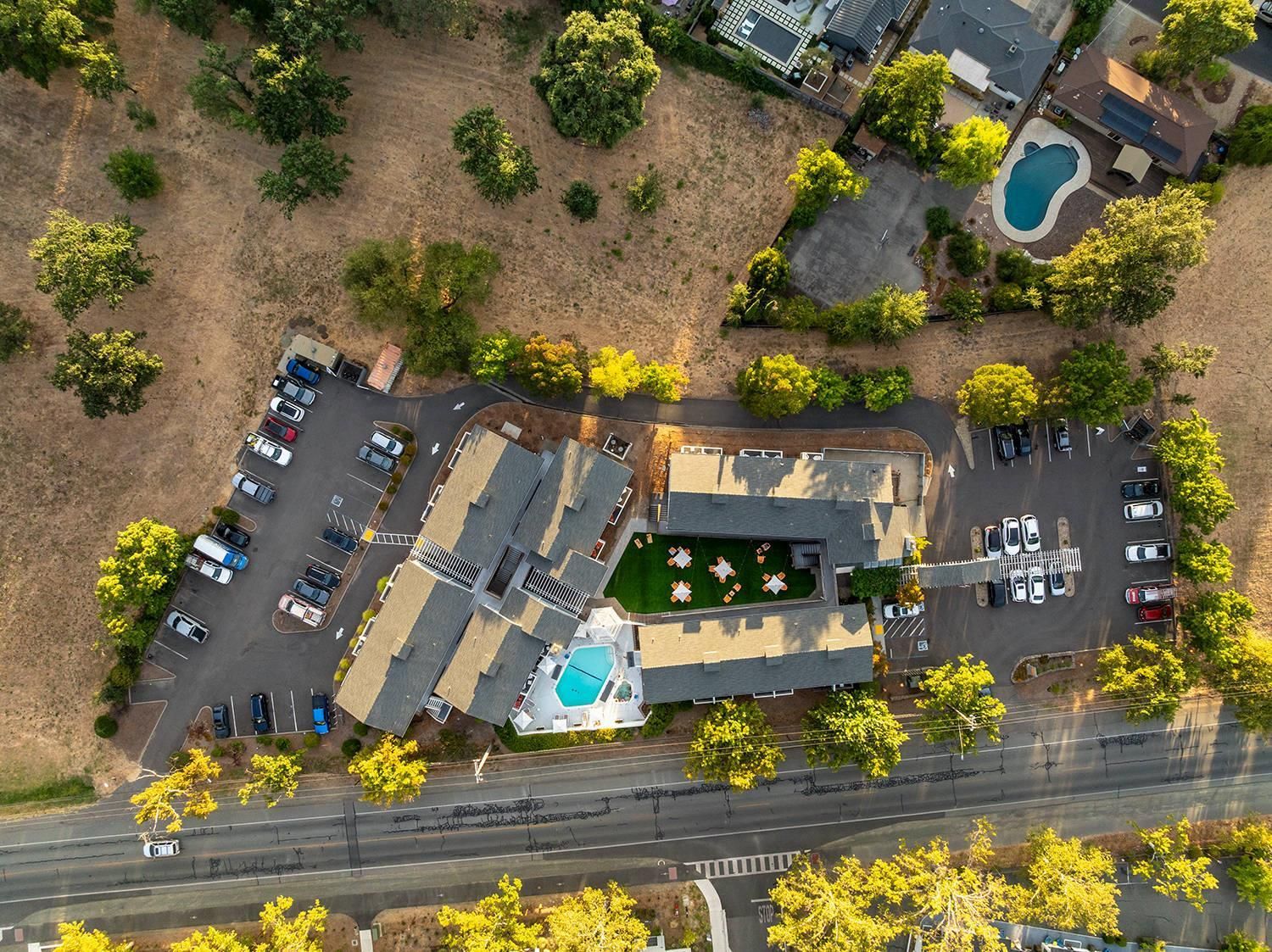 Vista aérea de uma propriedade com piscina, várias vagas de estacionamento e área ajardinada com árvores.