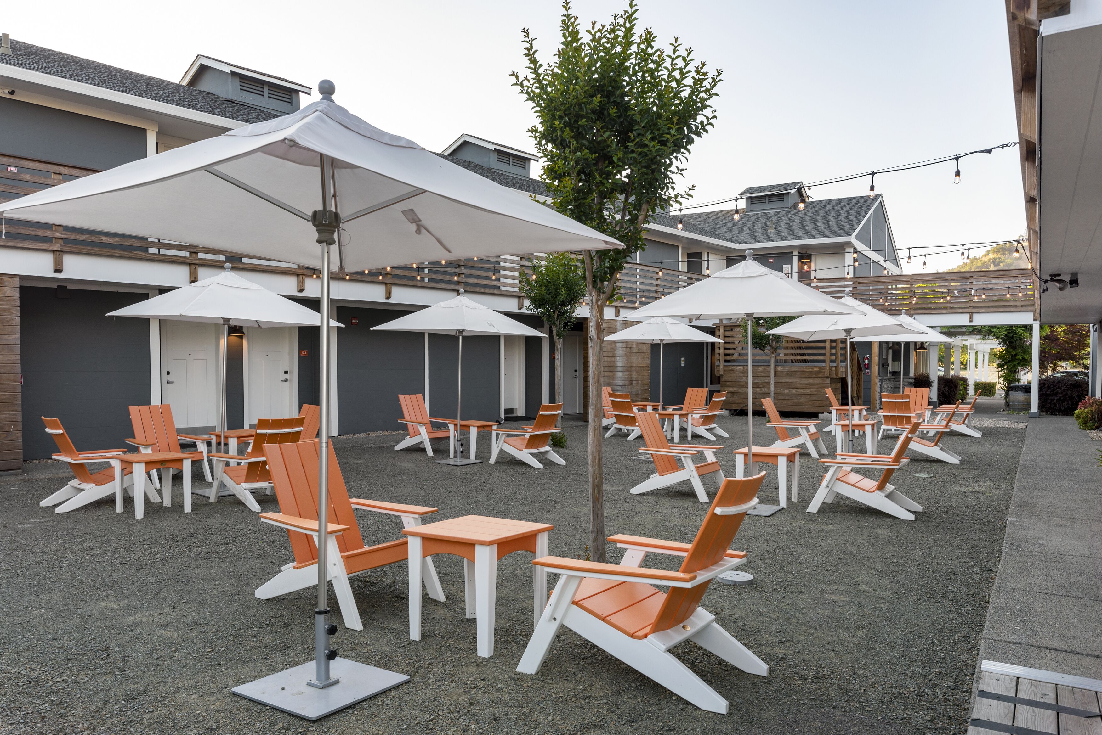 An outdoor seating area with white umbrellas and orange chairs, arranged in rows.