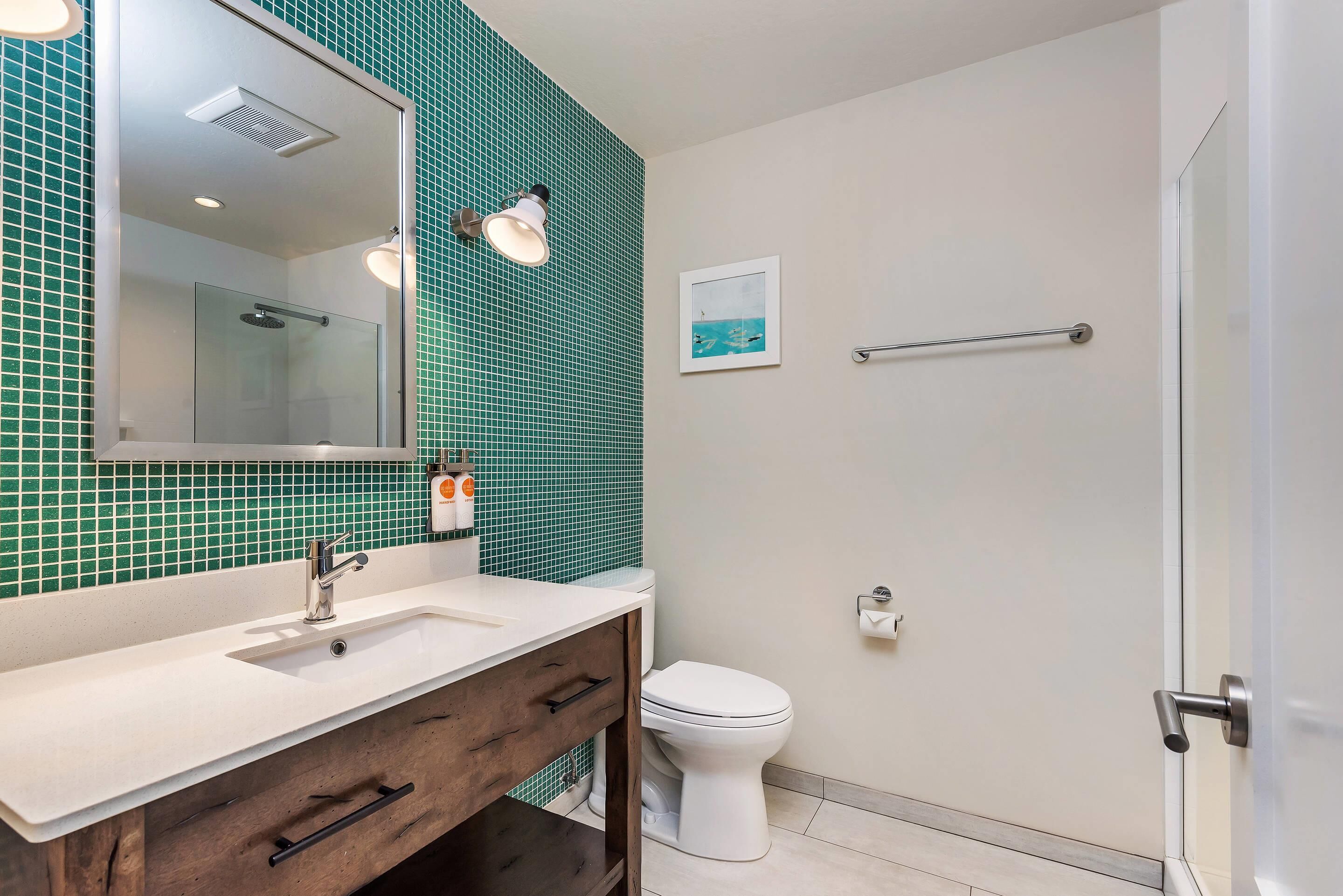 A bathroom with a white sink, a mirror, a glass-enclosed shower, and a toilet.