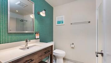 A bathroom with a white sink, a mirror, a glass-enclosed shower, and a toilet.