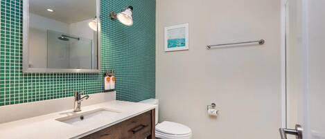 A bathroom with a white sink, a mirror, a glass-enclosed shower, and a toilet.