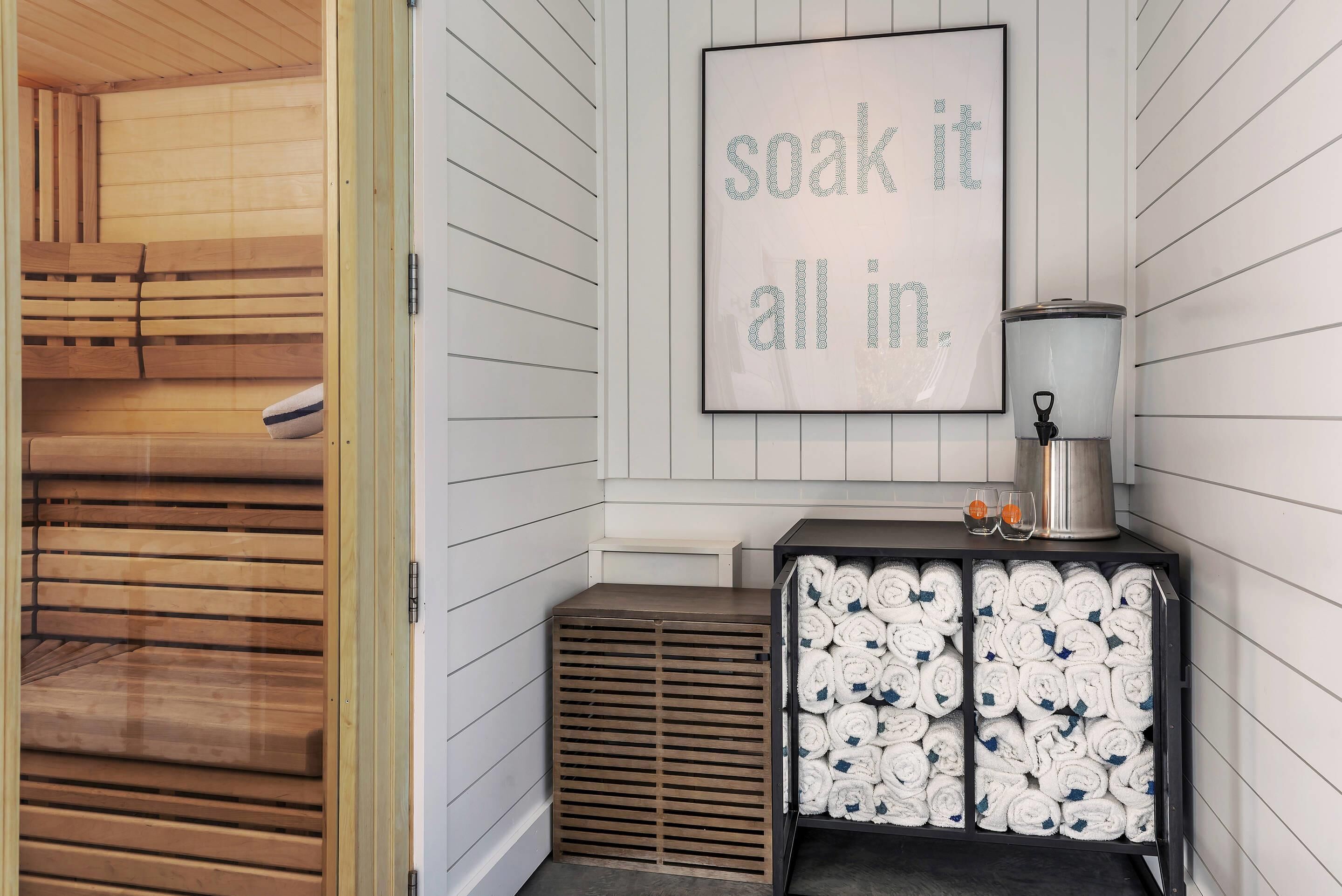 A sauna room with wooden benches, a towel rack with neatly rolled towels, and a framed motivational quote on the wall.