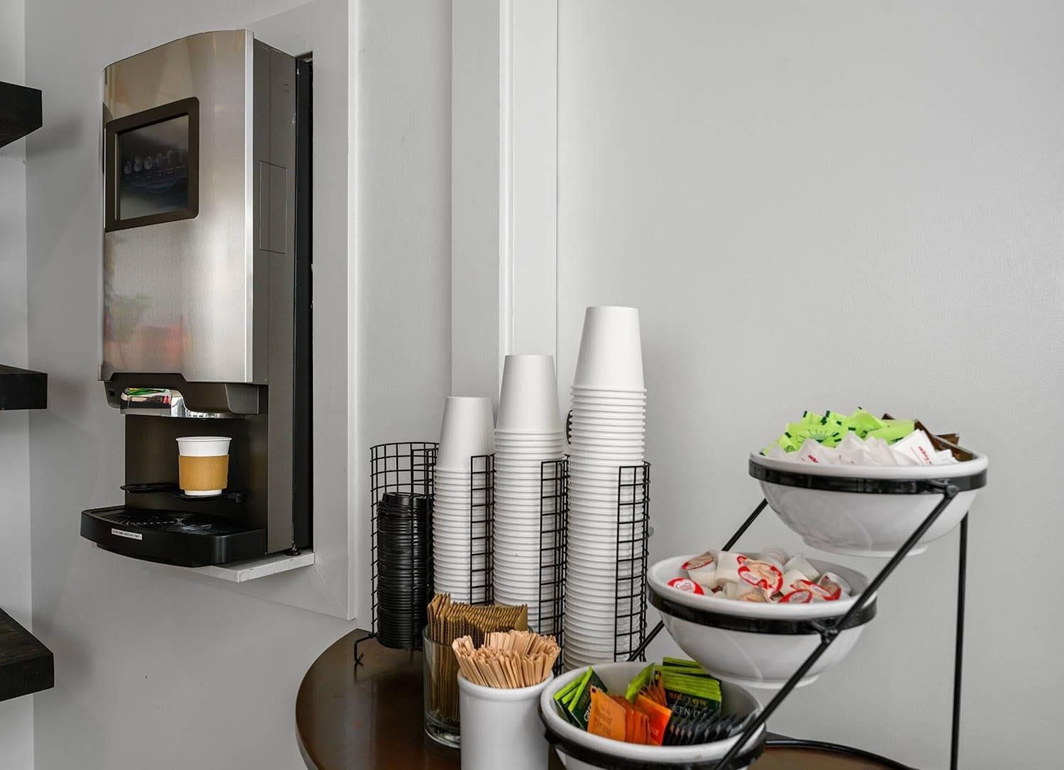 A modern room with a coffee machine, stacked white cups, and a buffet with various food items.