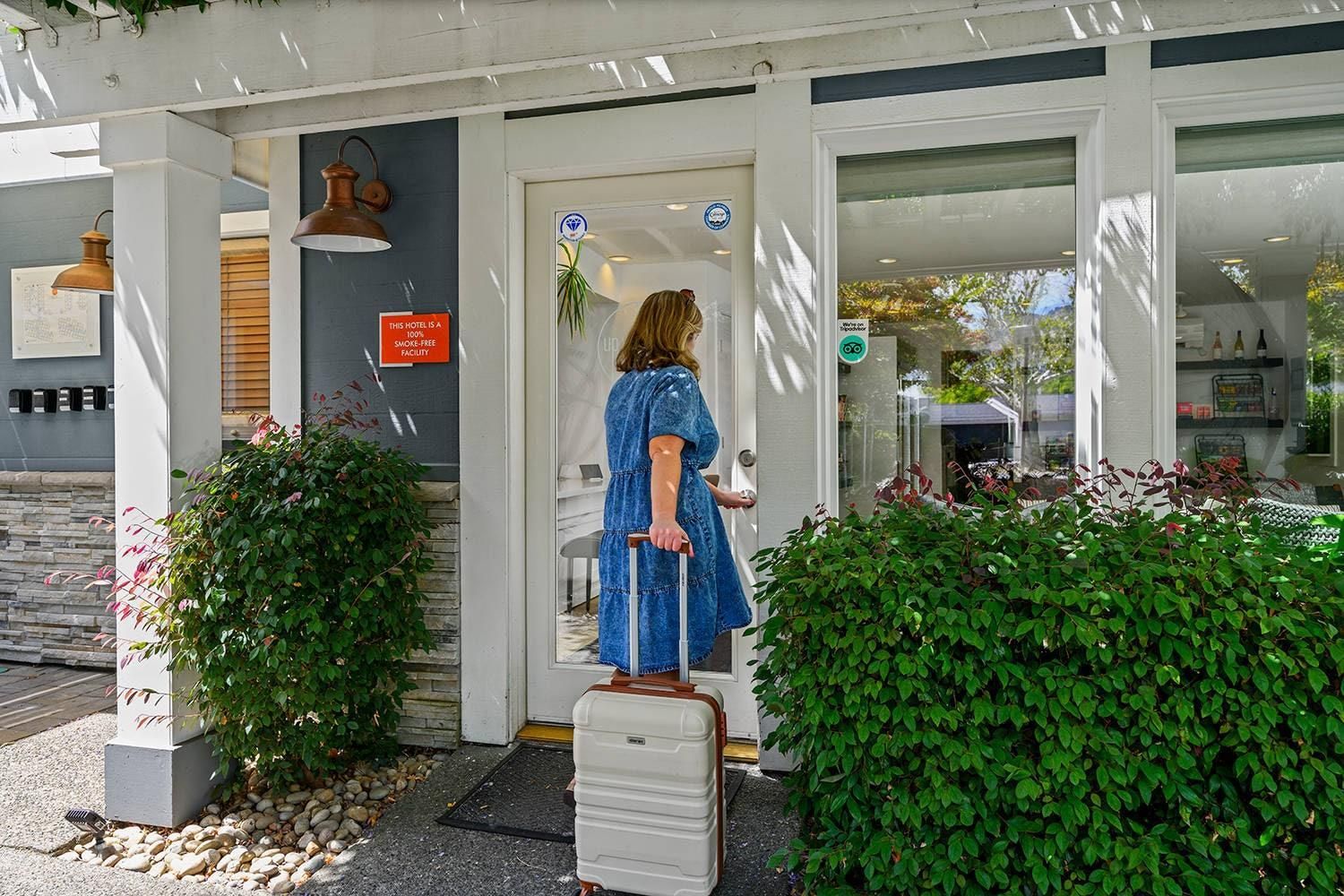 A woman in a blue dress exiting a hotel with a suitcase, a sign indicating the hotel is smoke-free, and a bike symbol suggesting bike parking.
