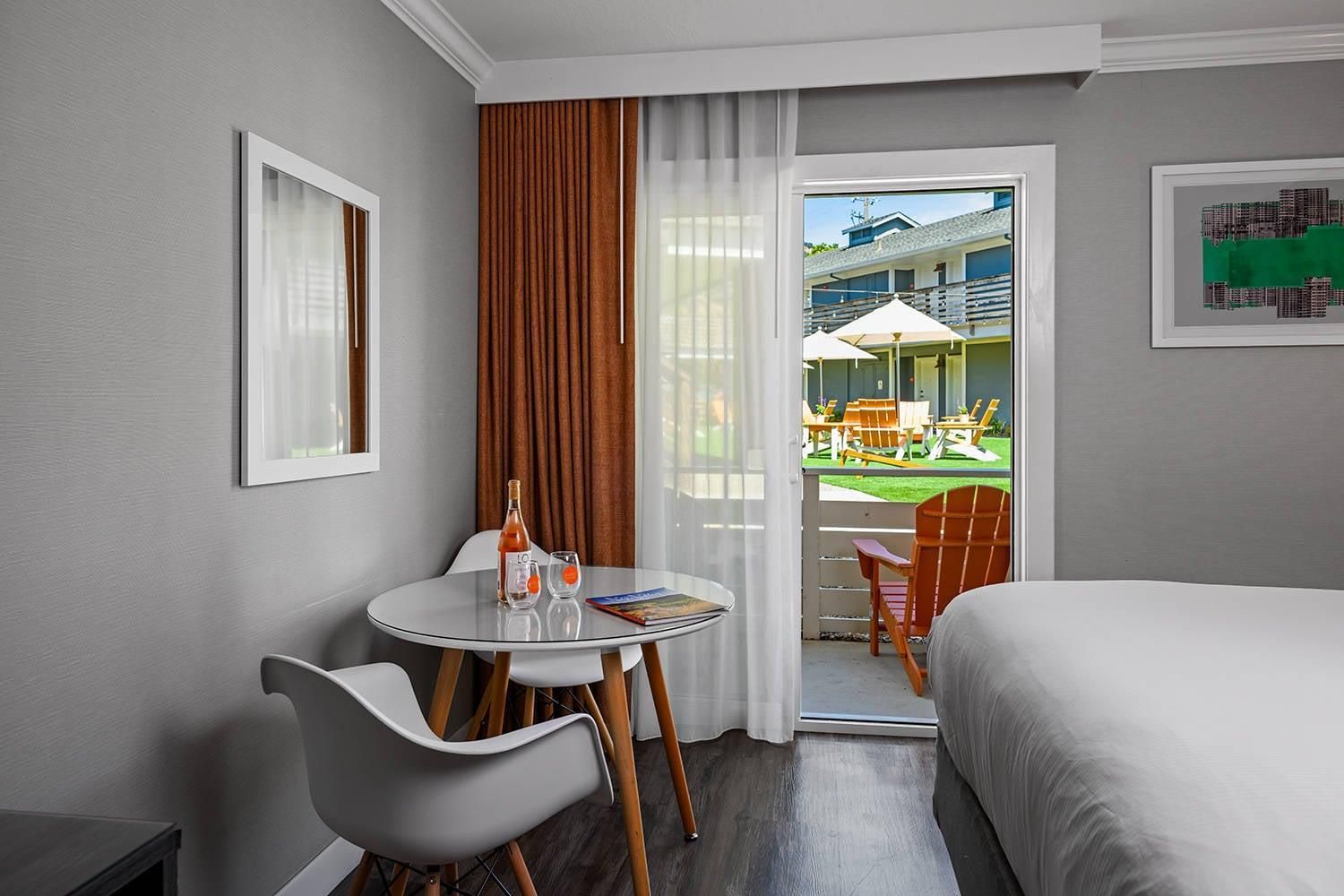 Habitación de hotel con cama, una mesa con sillas, ventana con cortinas y vista al área exterior.