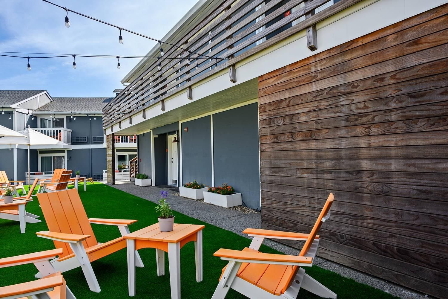An outdoor seating area with chairs and tables, a wooden wall, and a building with a balcony.