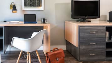 A modern office space with a desk, laptop, chair, television, and a briefcase.