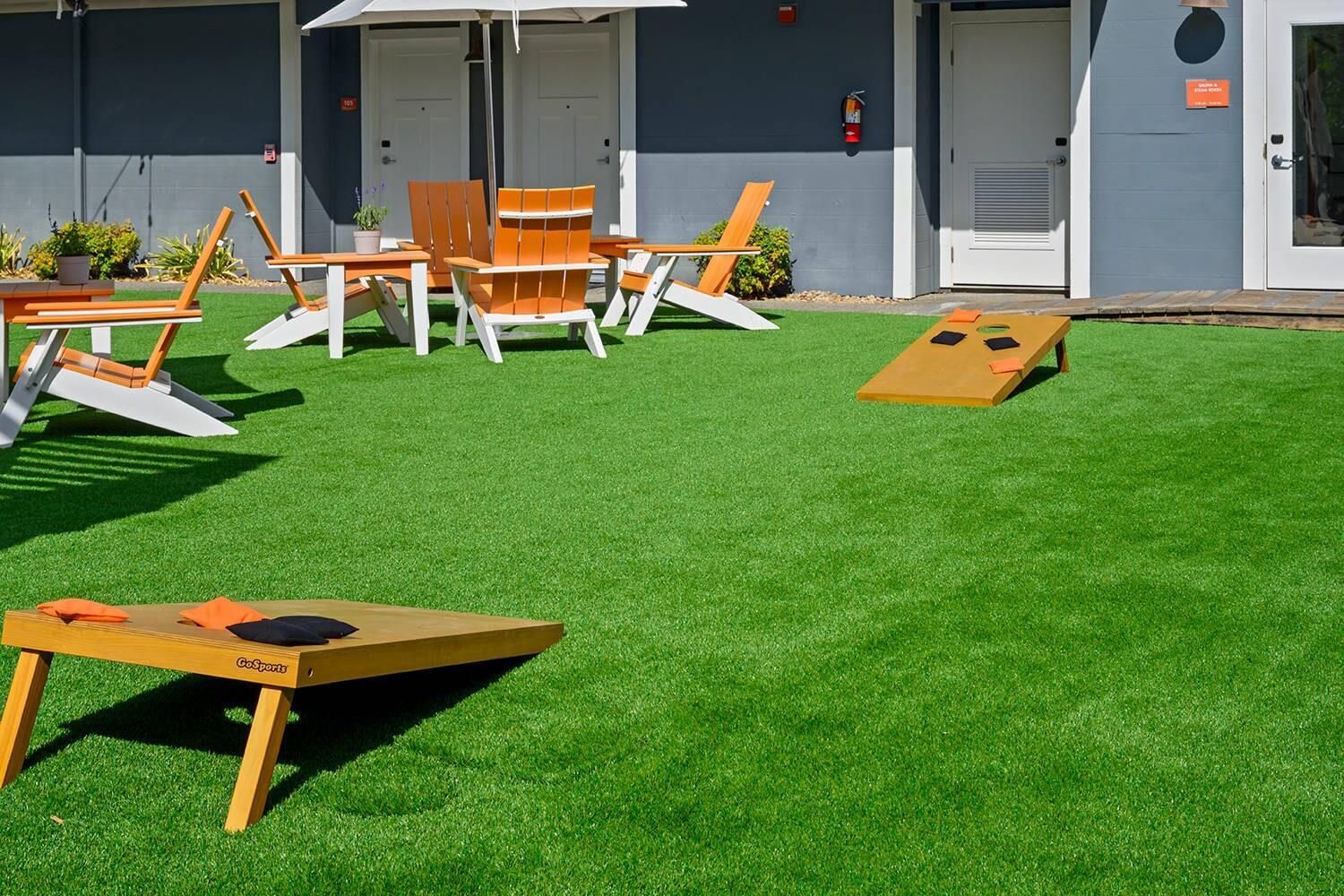 Een terras met kunstgras, houten lounge fauteuils en een tafel met kussens.