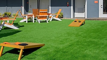 Een terras met kunstgras, houten lounge fauteuils en een tafel met kussens.