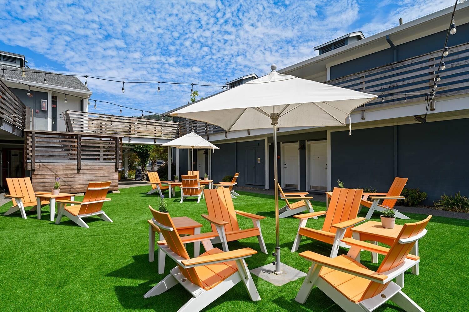 An outdoor seating area with chairs and tables, a grassy lawn, and a building with a modern design.