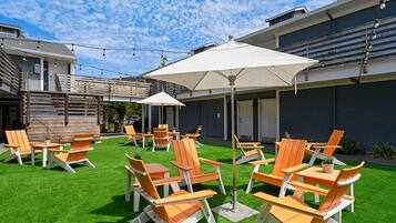 An outdoor seating area with chairs and tables, a grassy lawn, and a building with a modern design.