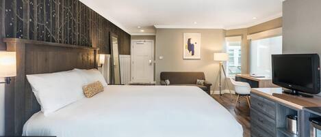 A modern hotel room with a large bed, a desk with a TV, and a view of the city.