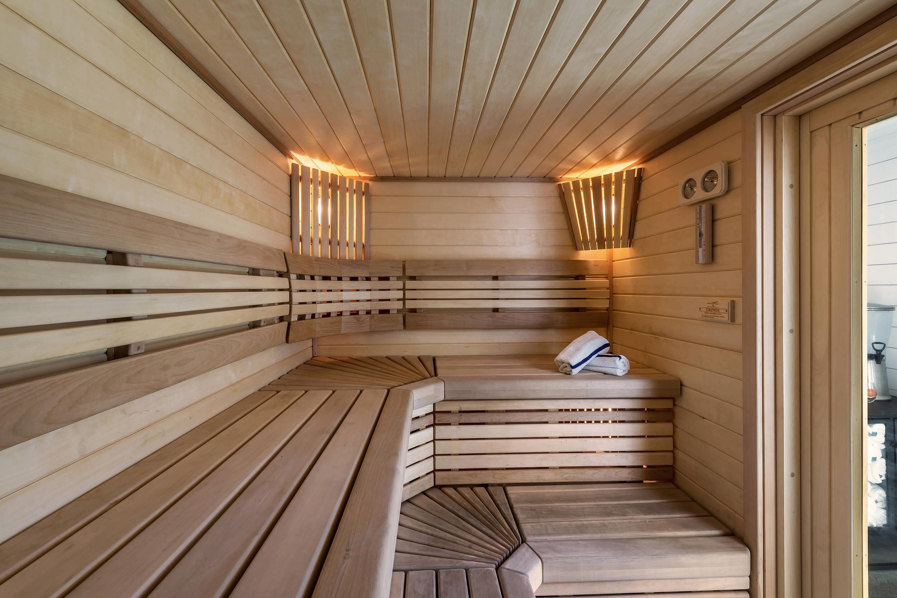 A sauna with wooden benches and slatted walls, a towel on one bench, and a thermometer on the wall.