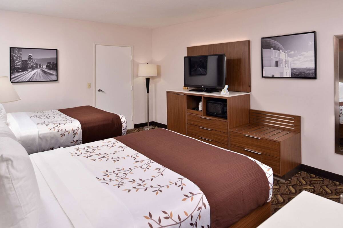 Ein Hotelzimmer mit zwei Betten, einem Fernseher auf einer Holzkommode und gerahmten Bildern an den Wänden.