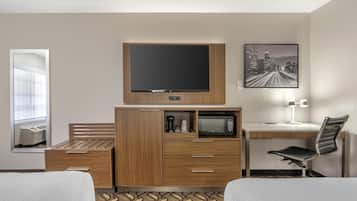 Et hotelværelse med seng, skrivebord med fladskærms-tv, mikrobølgeovn, lampe og stol.
