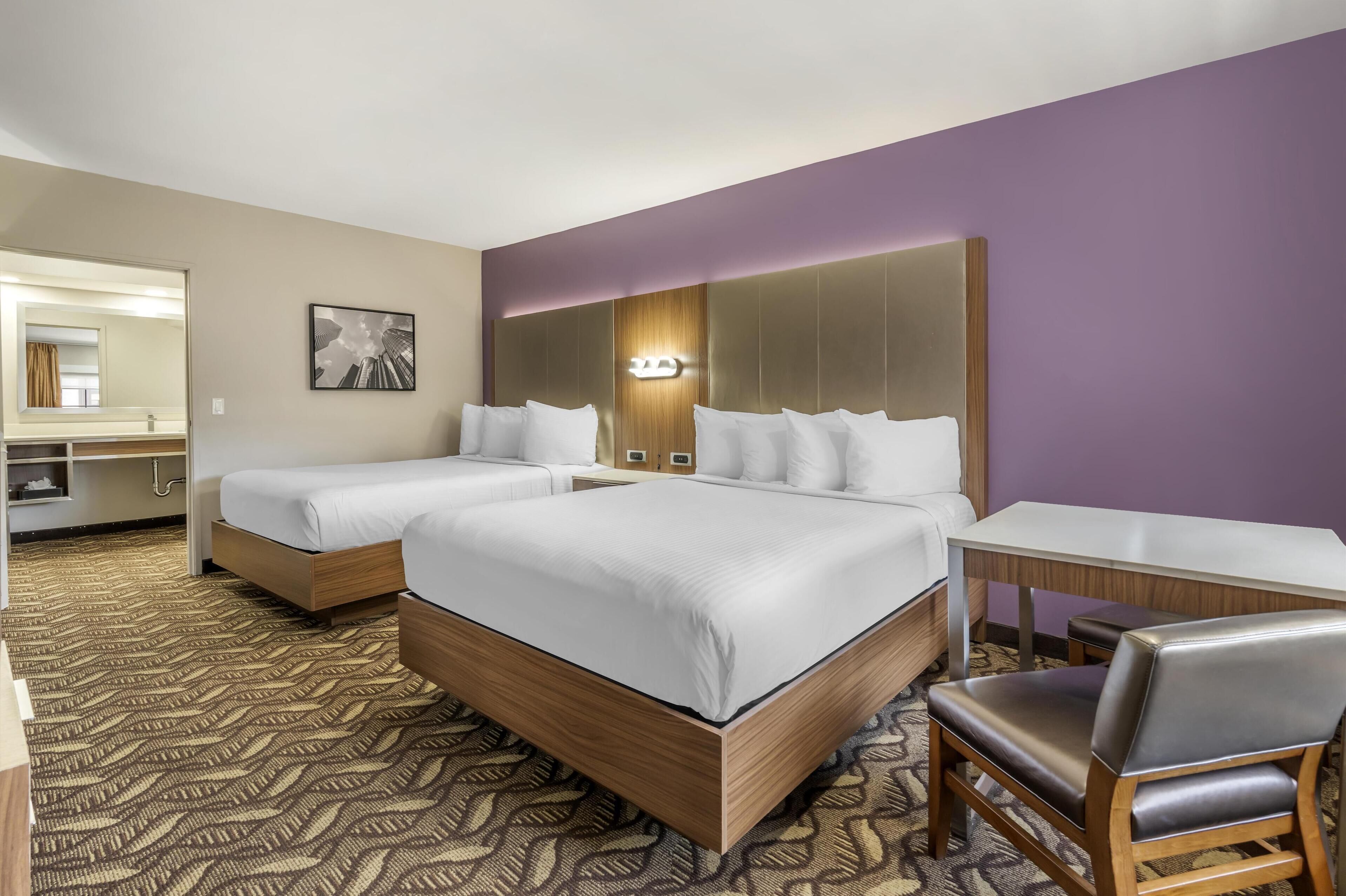 A hotel room with two beds, a desk, a chair, and a large mirror.