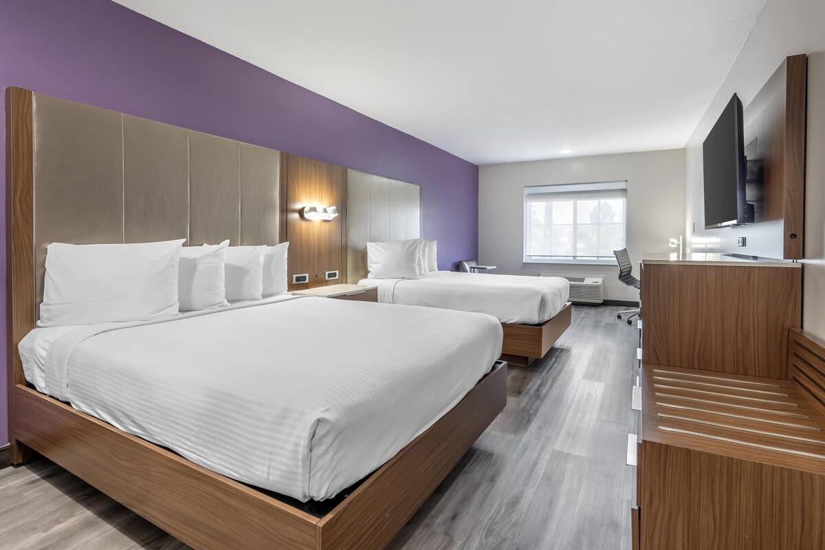 Ein modernes Hotelzimmer mit zwei Betten, einem Schreibtisch und einem Fernseher.