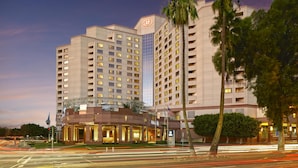 A multi-story hotel with a prominent logo, a well-lit entrance, and a parking area. - Hilton Long Beach Hotel (Long Beach)