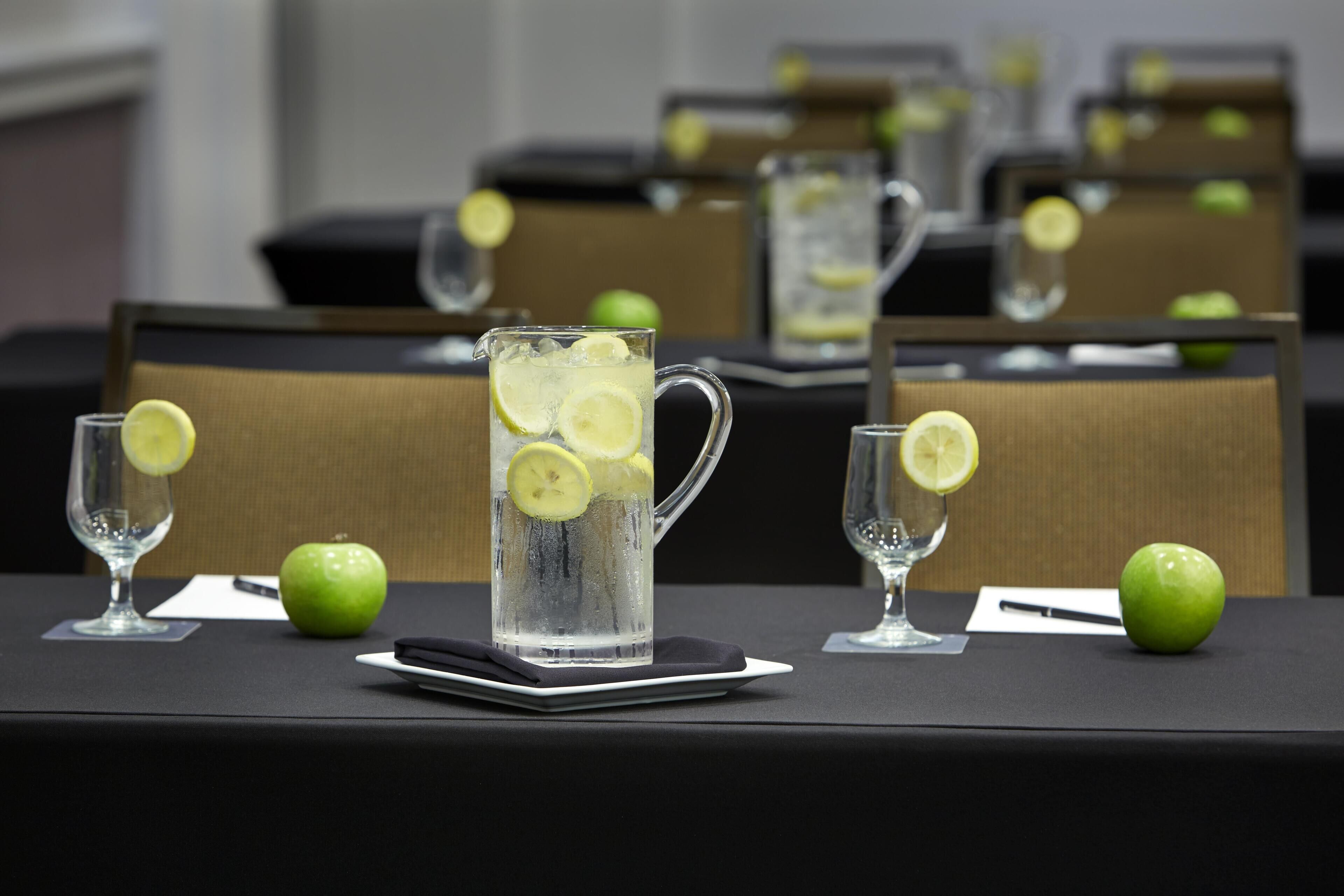 A table with a pitcher of water, glasses, and apples.