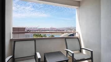 A balcony with two chairs and a small table, overlooking a harbor with cranes and a bridge.