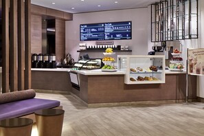 A modern café interior with a digital menu, a seating area, and a display case with pastries.