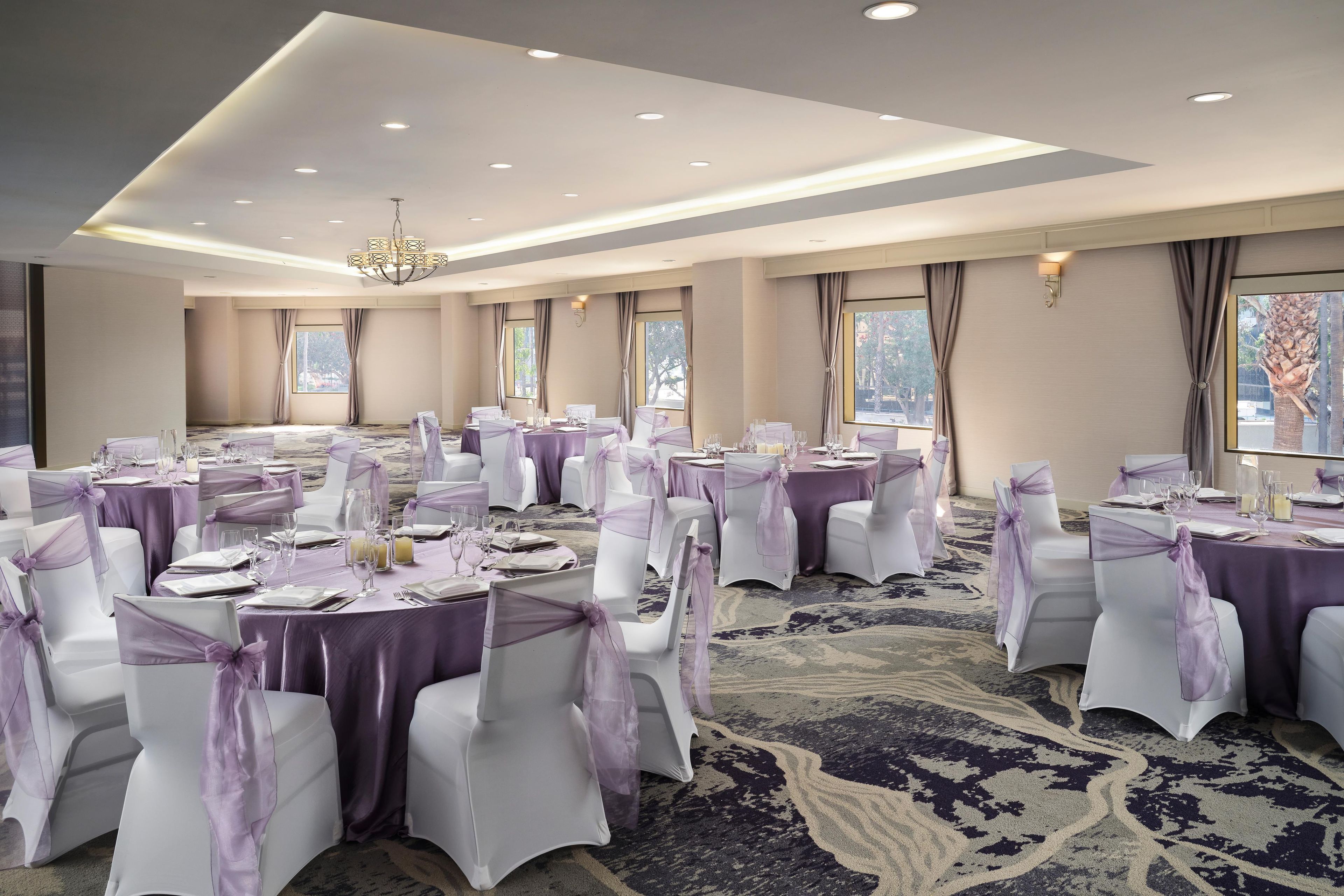 A banquet hall with round tables, white chairs, and purple decorations.