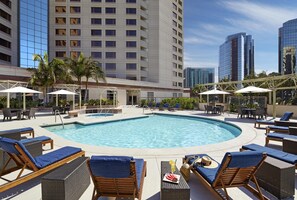 A rooftop pool with lounge chairs and umbrellas, surrounded by tall buildings.