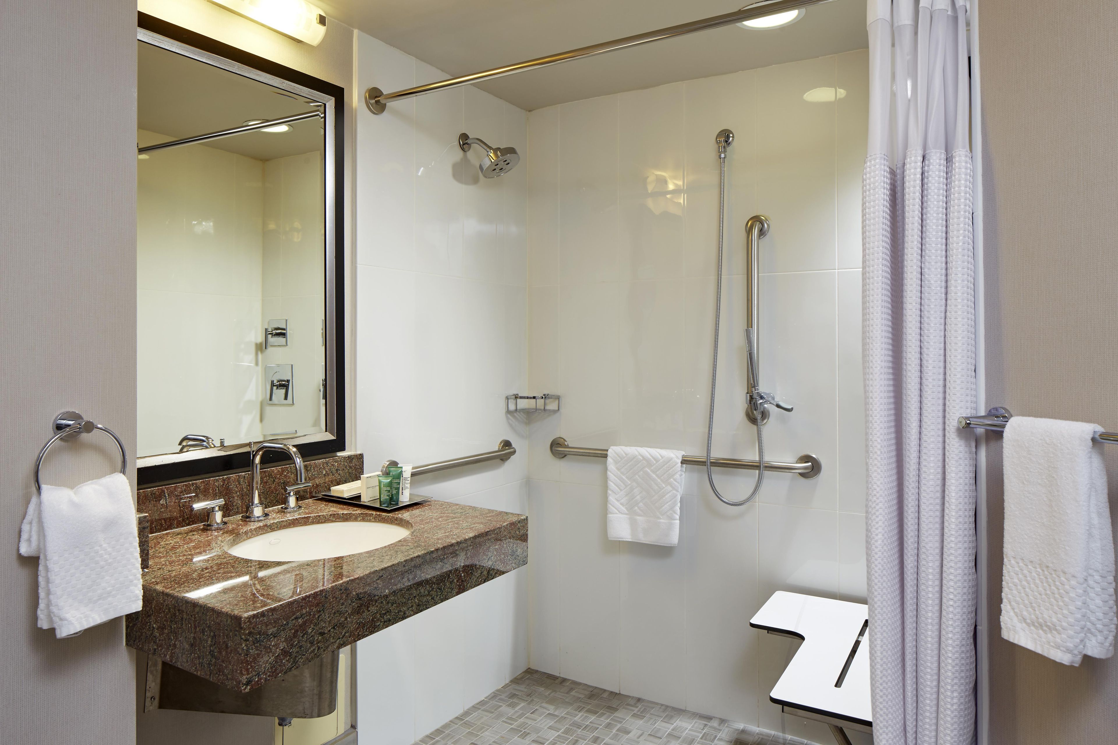 Une salle de bain d’hôtel équipée d’un lavabo, d’un miroir, d’une douche et d’un porte-serviettes.