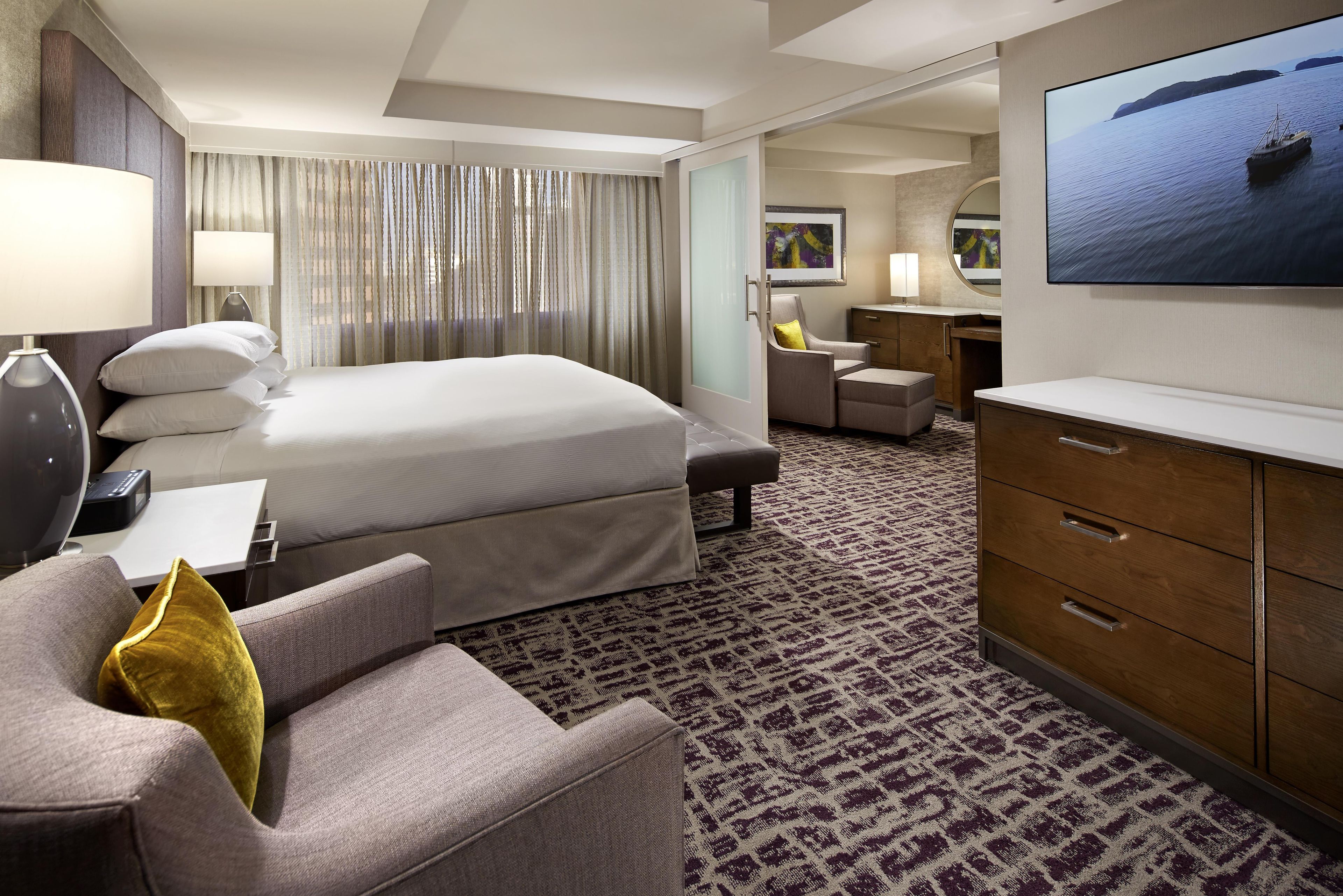 A hotel room with a bed, a desk, a chair, a TV, and a view of the sea.