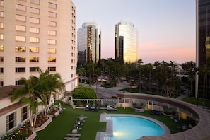 A hotel with a pool, palm trees, and modern buildings in the background.