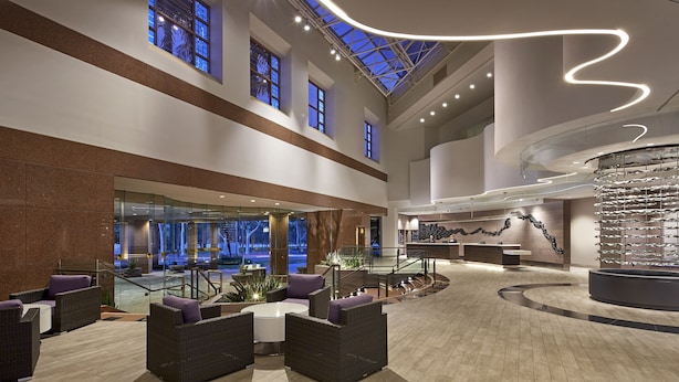 A spacious lobby with a high ceiling, large windows, and a central seating area with chairs and a table. - Hilton Long Beach Hotel (Long Beach)