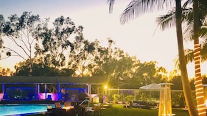 An outdoor pool area with lounge chairs and tables, surrounded by greenery and palm trees. - Hilton Long Beach Hotel (Long Beach)