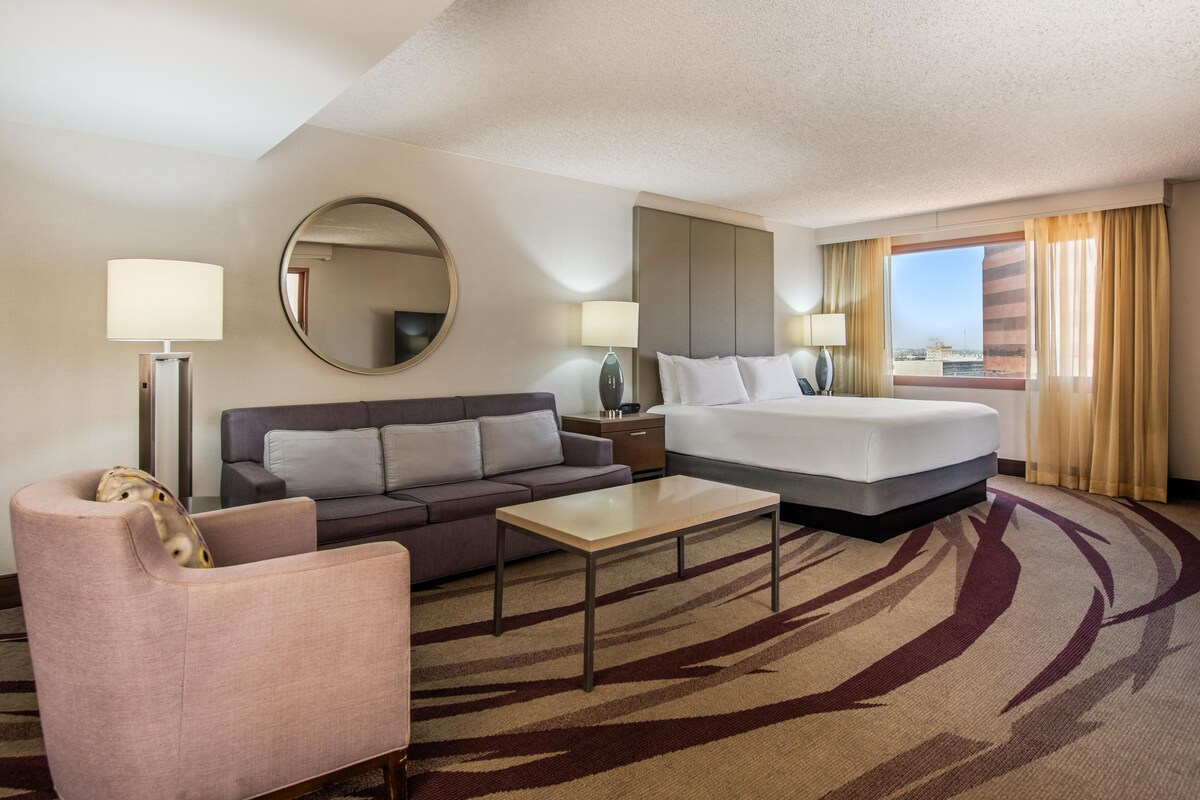 Una habitación de hotel con una cama, un sofá, una silla, una mesa de centro y un espejo grande.