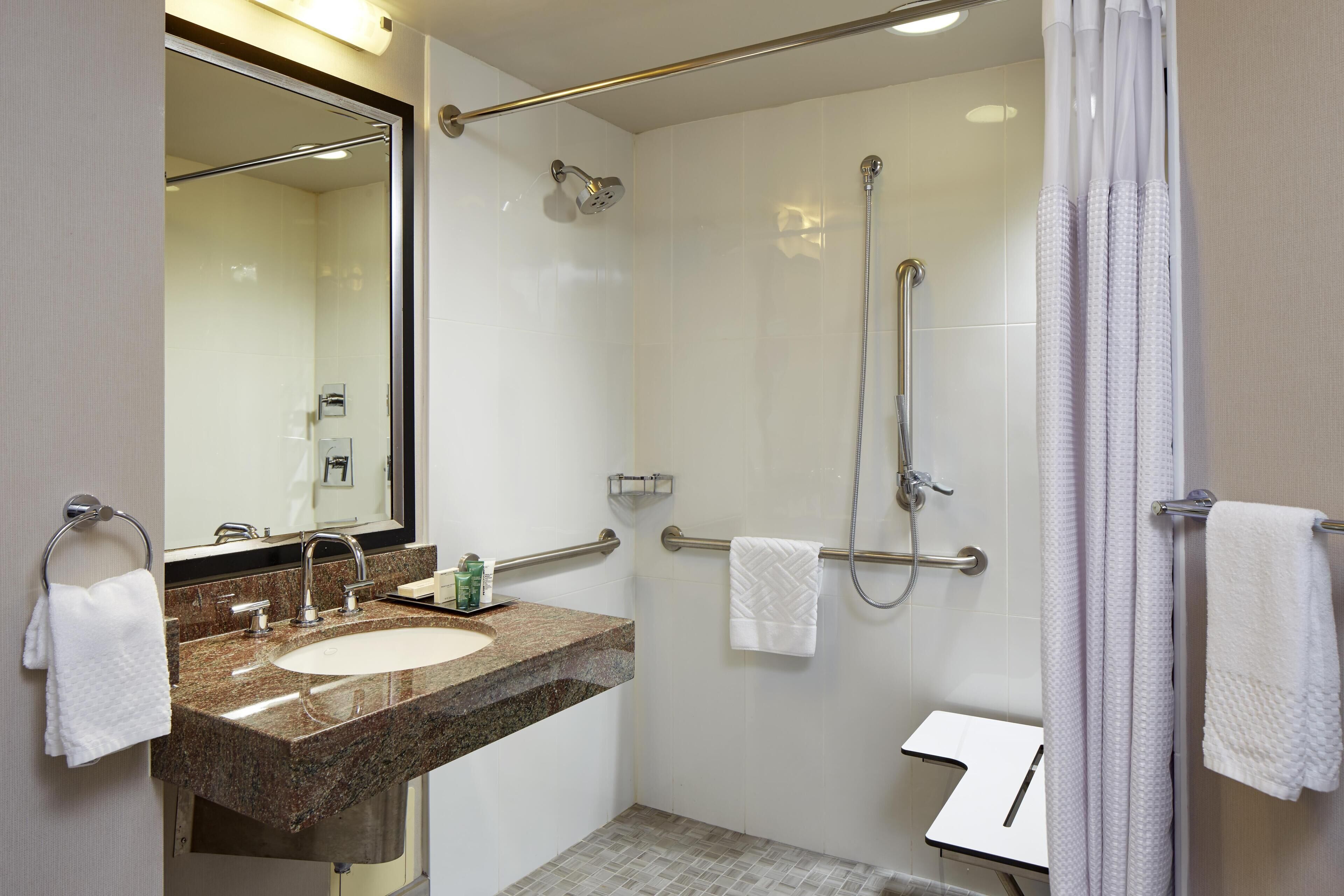 A bathroom with a sink, mirror, shower, and towel rack.