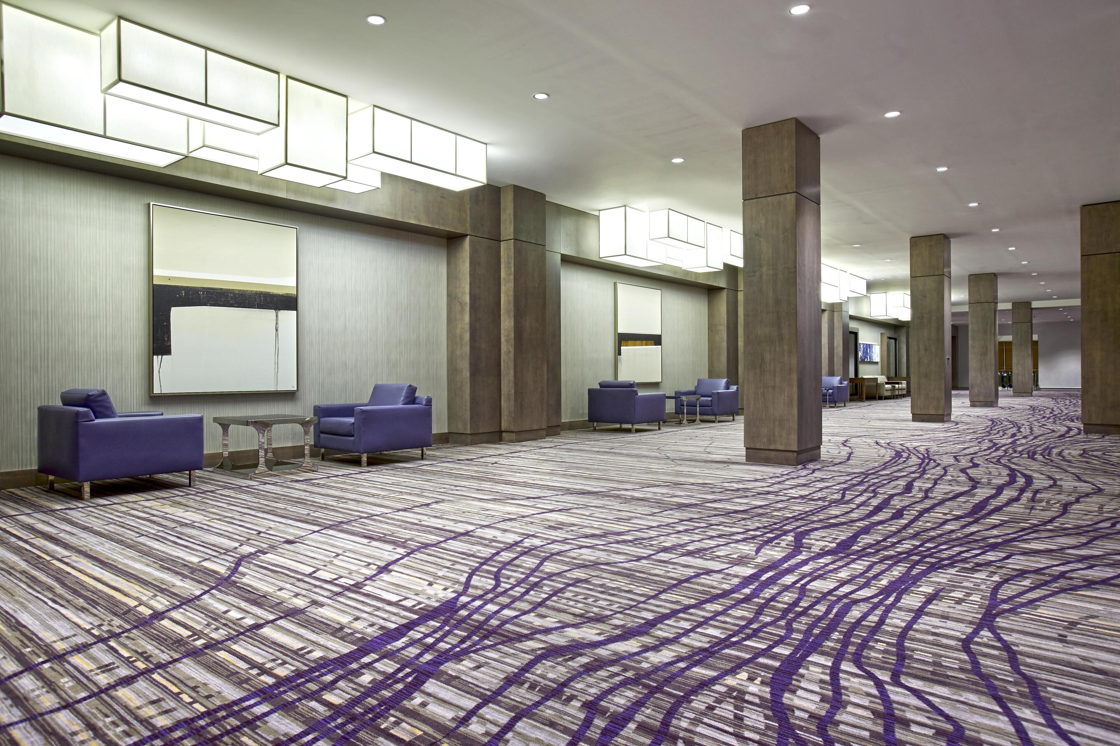 Un vestíbulo de hotel espacioso con alfombra estampada, zonas de estar y grandes pilares.