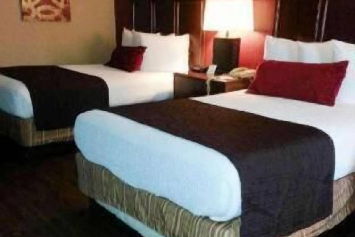 Quarto de hotel com duas camas, uma mesa de cabeceira com abajur e um quadro na parede.
