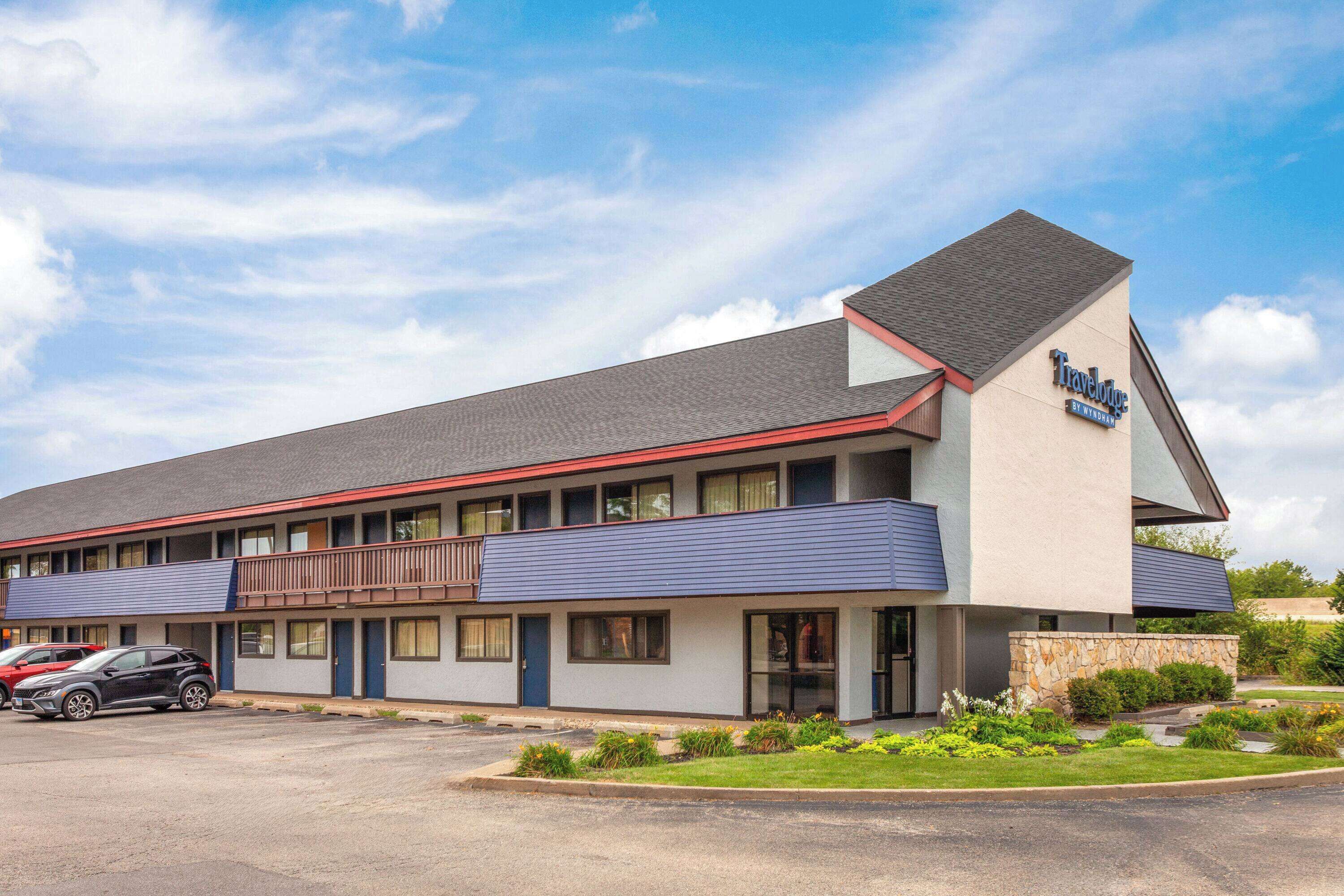 A Travelodge motel with a two-story structure, a parking lot, and a landscaped front yard.