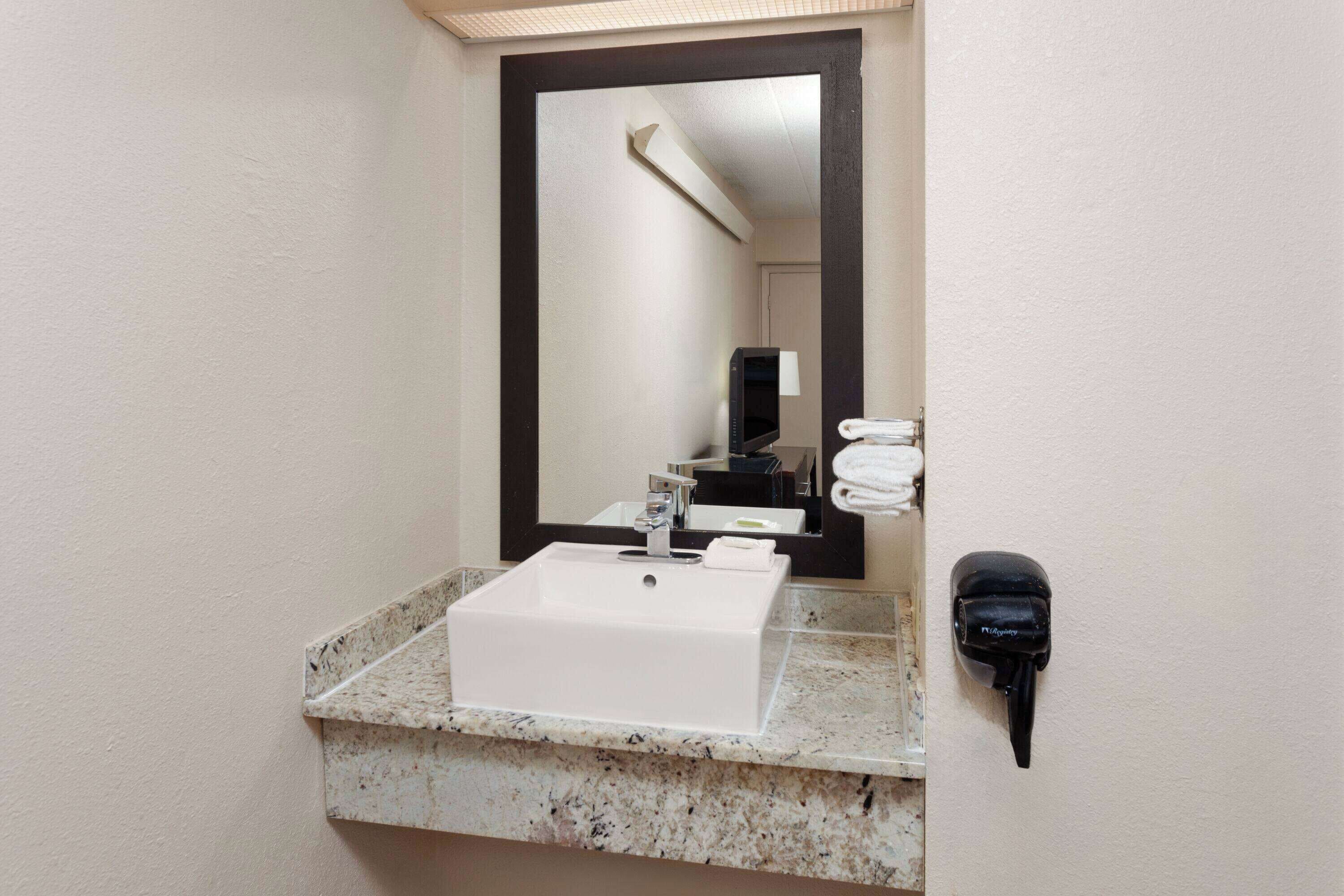 A bathroom with a white sink, a mirror, and a hairdryer mounted on the wall.