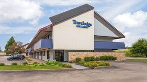 A Travelodge by Wyndham hotel with a stone facade, a sloped roof, and a parking lot. - Travelodge by Wyndham Peoria (Peoria)