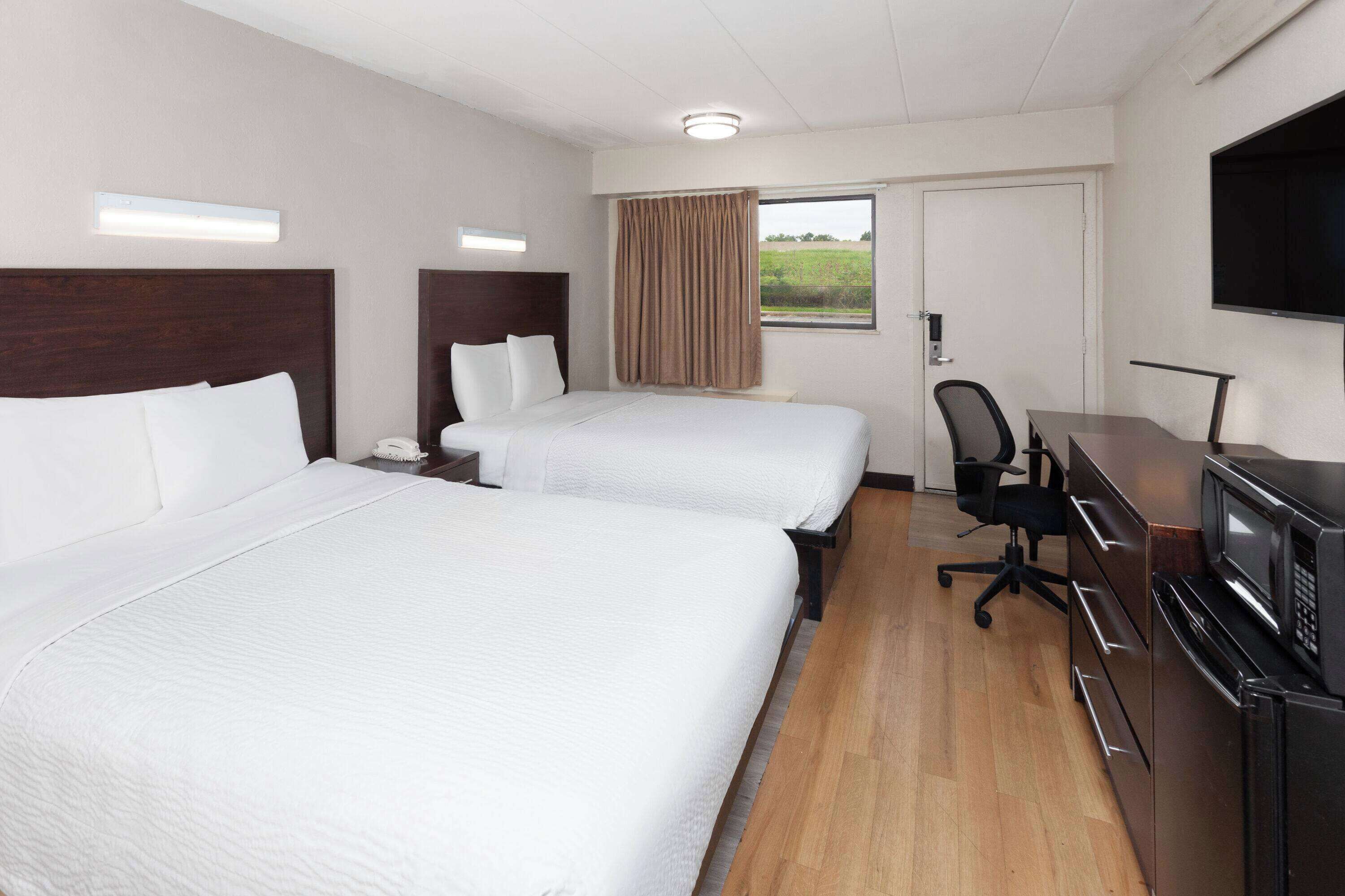 A hotel room with two beds, a desk with a computer, a TV, and a window with curtains.