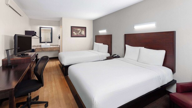 A hotel room with two beds, a desk with a computer, a chair, and a small table. - Travelodge by Wyndham Peoria (Peoria)