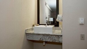 A bathroom with a white sink, a mirror, and a towel rack. - Travelodge by Wyndham Peoria (Peoria)
