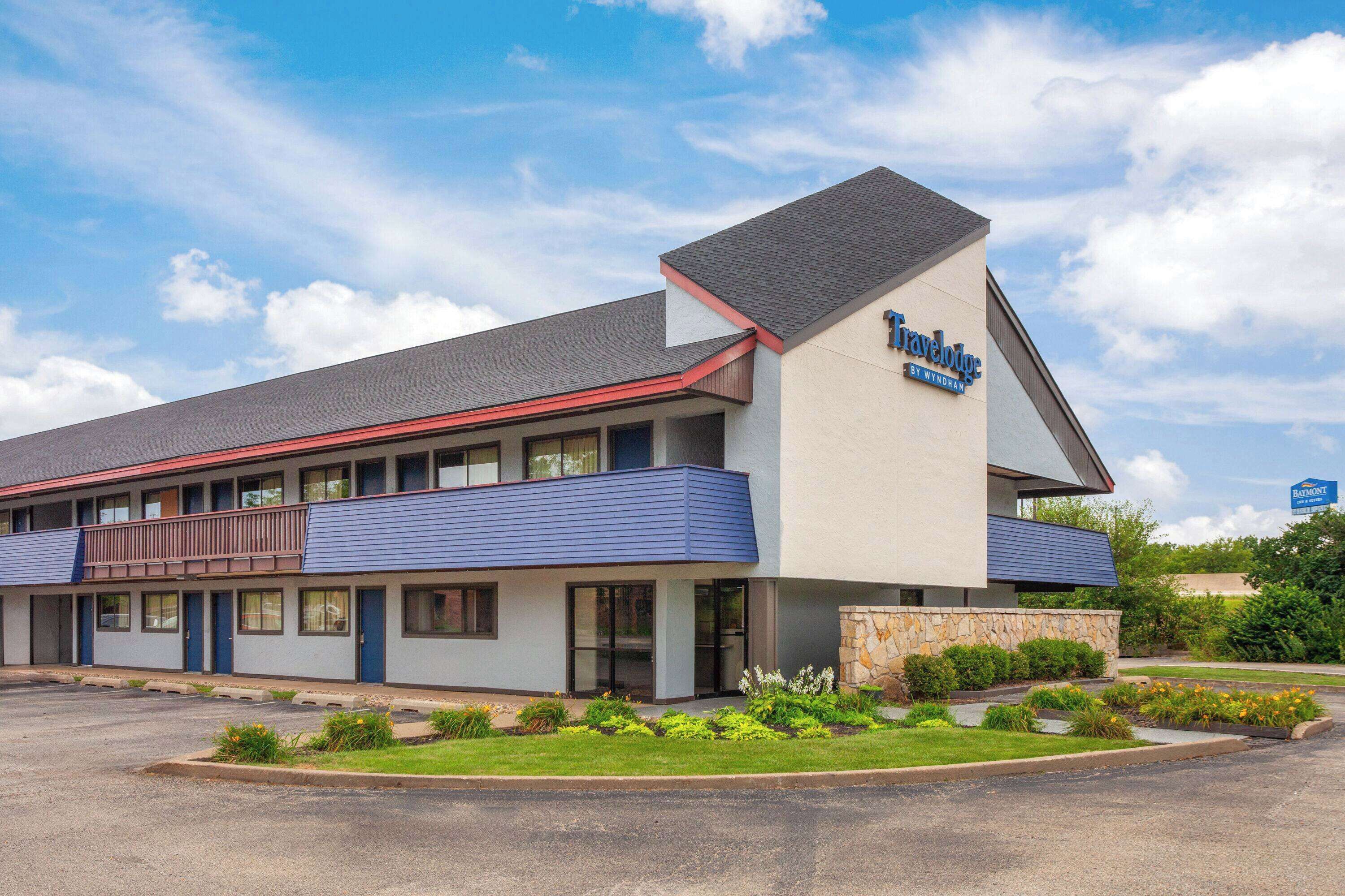 Un hotel Travelodge dal design moderno, con tetto piano, un balcone al secondo piano e un'area giardino ben curata di fronte.