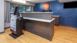 A reception desk with a computer and a cash register, a window with curtains, and a blue wall with a painting. - Travelodge by Wyndham Peoria (Peoria)