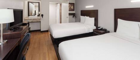 A hotel room with two beds, a desk with a computer, a TV, and a bathroom with a mirror and sink.