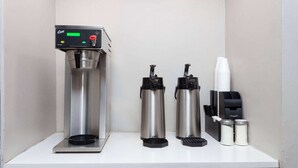 A coffee machine, two thermos flasks, disposable cups, and condiment containers on a counter. - Travelodge by Wyndham Peoria (Peoria)