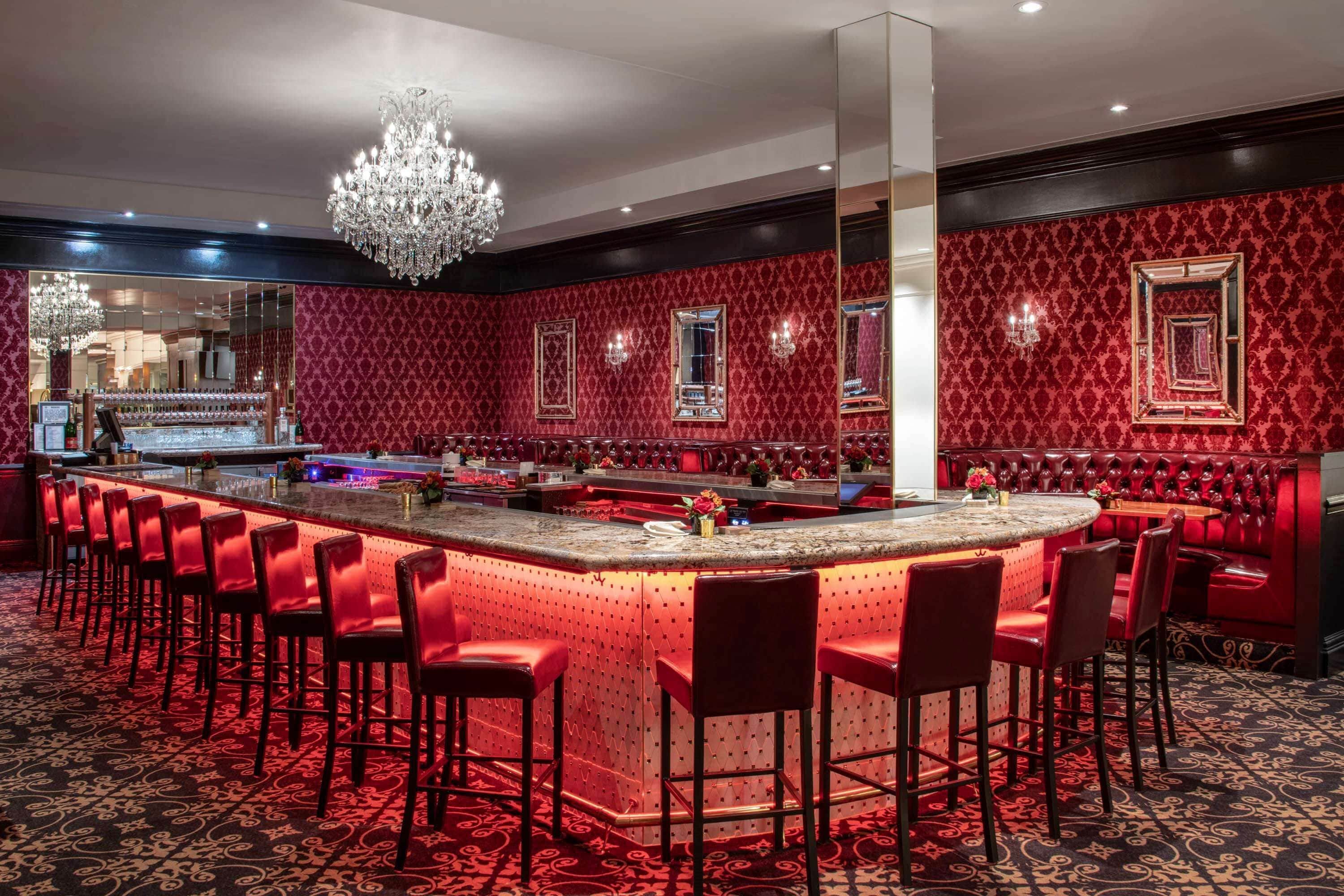 Un espace bar avec un mur aux motifs rouges et noirs, un comptoir central et de nombreux tabourets de bar rouges.