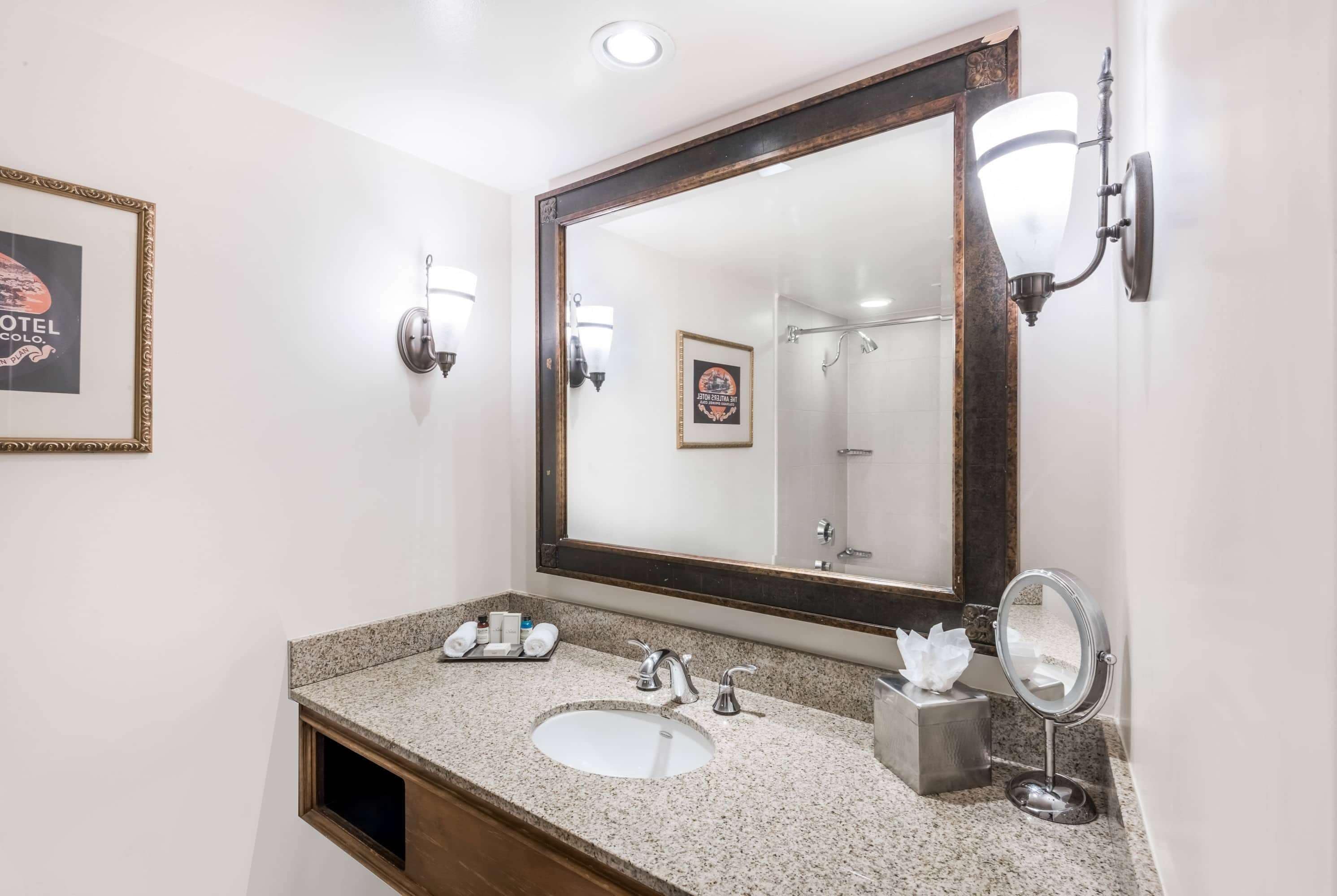 A hotel bathroom with a large mirror, a sink, a vanity, and a towel rack.